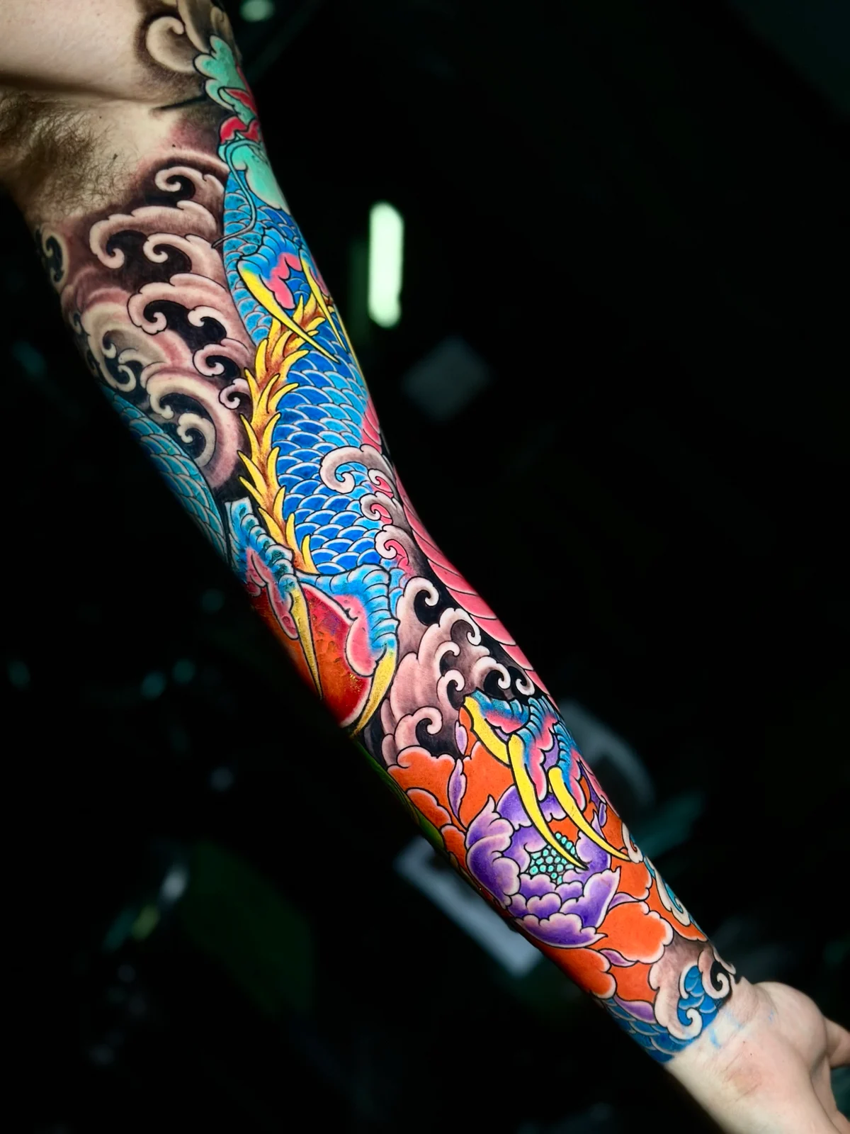 Vibrant Japanese colour sleeve featuring a coiled blue dragon, a purple peony, and traditional black wind-bar shading at Bloodline Tattoo Phuket.