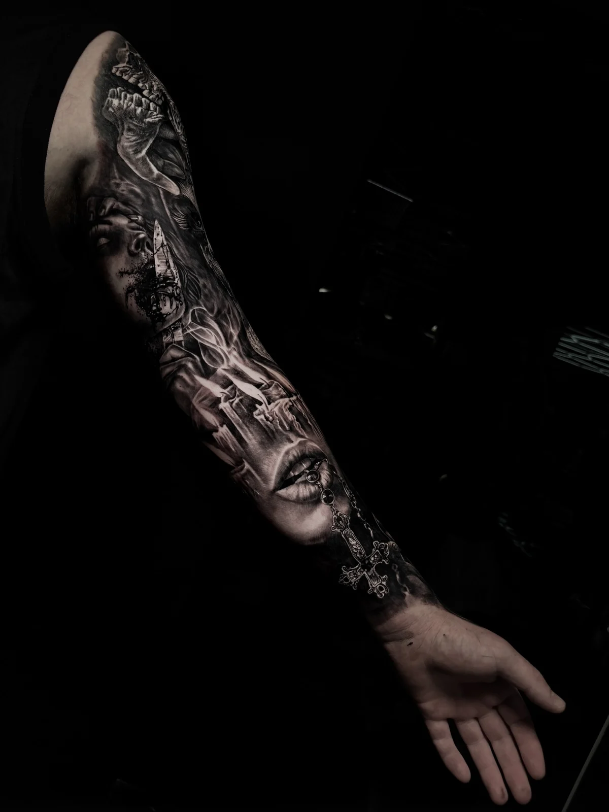 Dark realism full sleeve with haunted portrait, melting candles, and rosary cross at the wrist in black and grey at Bloodline Tattoo Phuket.