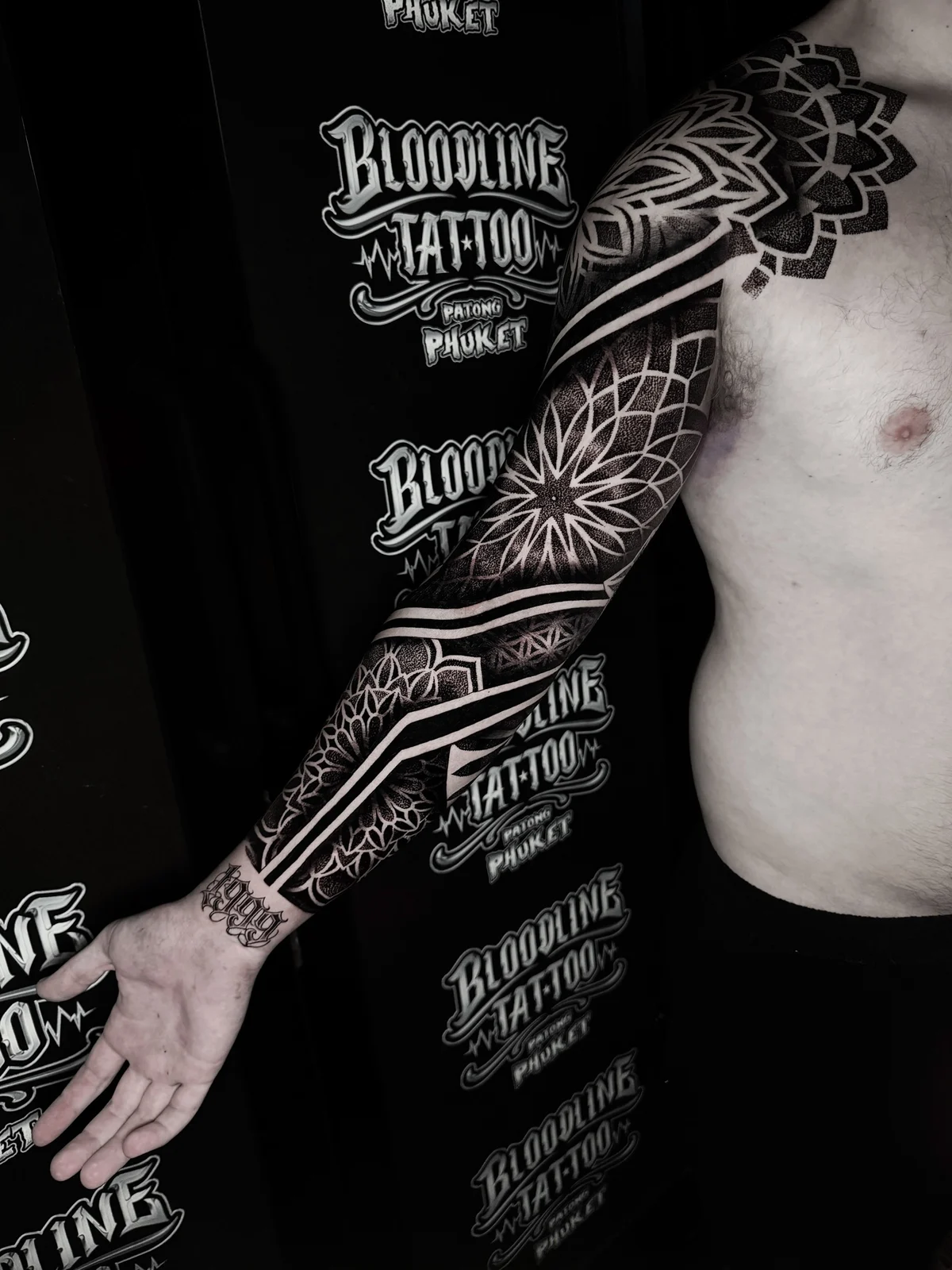 Geometric mandala and dotwork blackwork full sleeve with bold negative-space bands on the arm at Bloodline Tattoo Phuket.