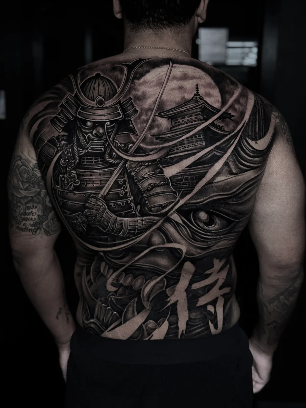 Japanese black and grey full-back piece with armored samurai, pagoda under a full moon, Hannya mask, and kanji at Bloodline Tattoo Phuket.