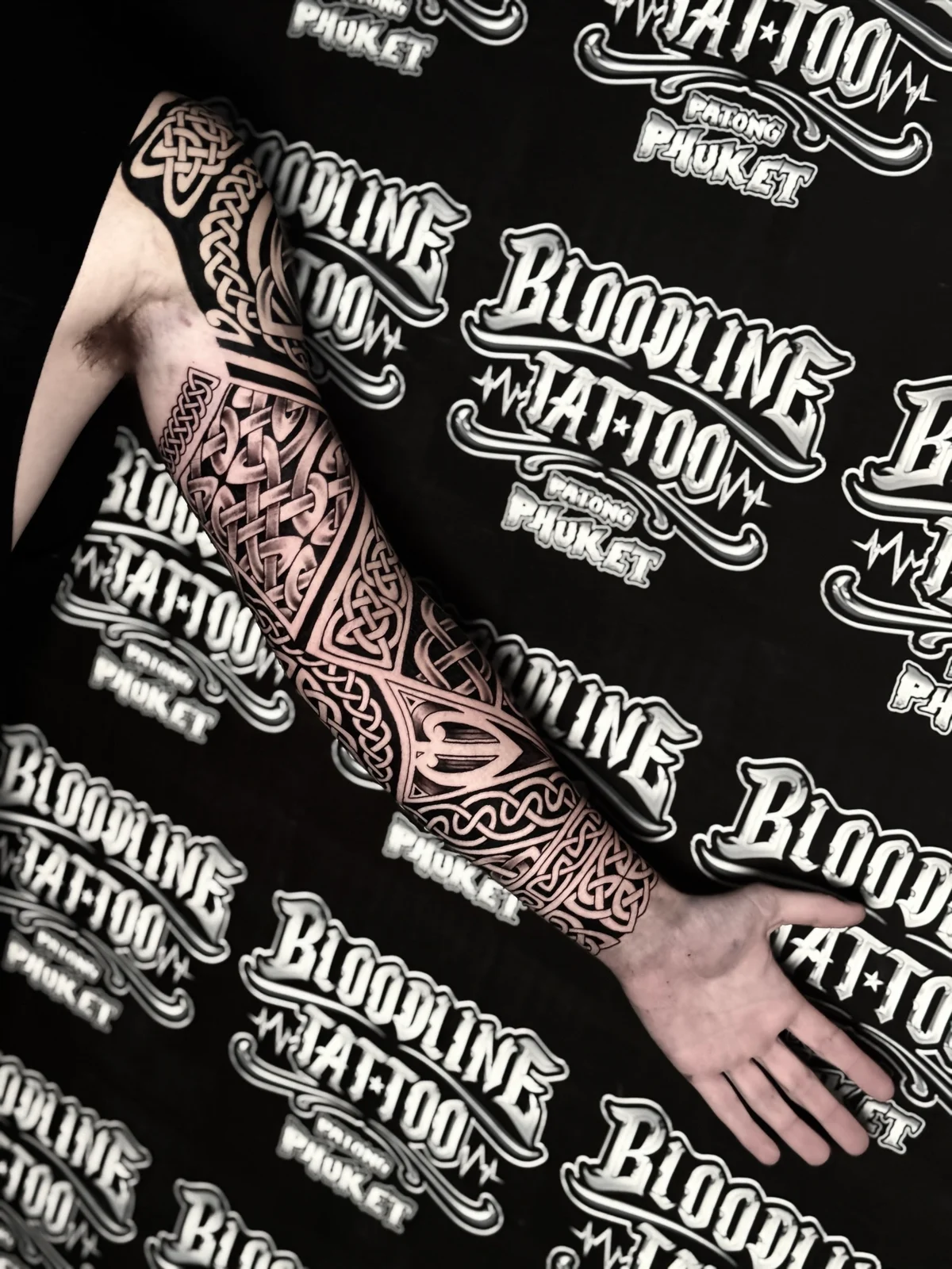 Intricate Celtic braid and geometric knotwork full sleeve with bold outlines and woven negative-space patterns from shoulder to wrist, at Bloodline Tattoo Phuket.
