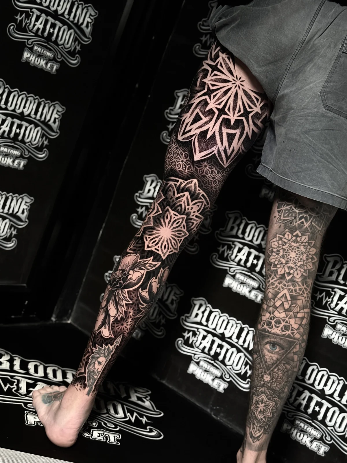 Symmetrical dual full leg mandala sleeves featuring thigh lotus mandalas, geometric honeycomb bands, and an all-seeing eye inside a triangle on the calf, at Bloodline Tattoo Phuket.