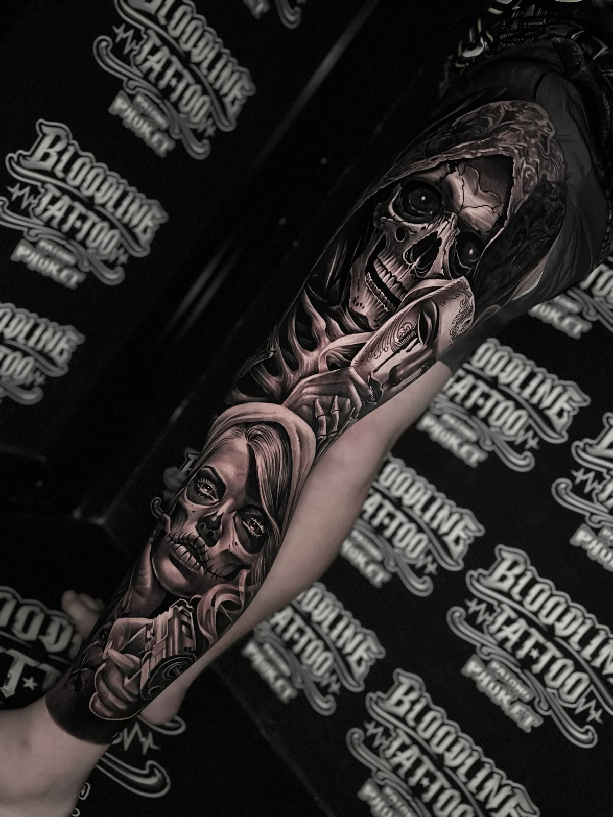 Detailed black and grey realism full leg sleeve tattoo featuring a hooded skull, Venetian mask, Santa Muerte woman, and handgun at Bloodline Tattoo Phuket.